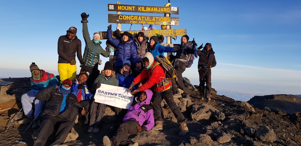 Trekkers celebrating at Uhuru Peak, the summit of Mount Kilimanjaro, at sunrise.